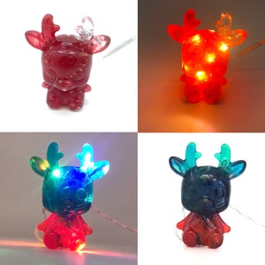 May include: A set of four decorative reindeer figurines with internal LED lights. The reindeer are red, blue, and clear, with illuminated antlers. The lights cycle through various colors, creating a festive holiday display.