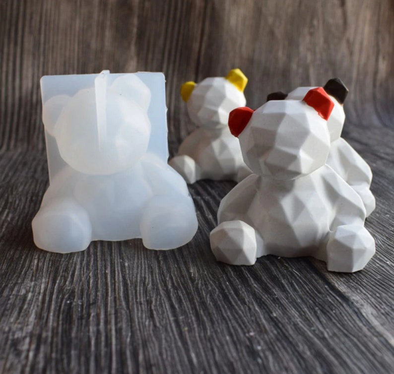 May include: A clear silicone mold and several white geometric bear figurines with colored ears. The bears have yellow, red, and black accents. The mold is in the shape of a bear.