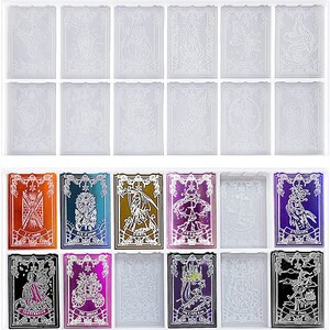 May include: A collection of tarot card molds in a clear tray. The molds feature intricate designs of various figures and symbols. Some cards have metallic foil accents in colors like orange, blue, and purple. The cards are rectangular with decorative borders.