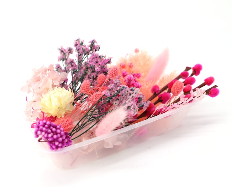 May include: A clear plastic rectangular container filled with an assortment of dried flowers and grasses in shades of pink, magenta, and cream. The arrangement includes pussy willow branches, fluffy bunny tails, and small clusters of statice.
