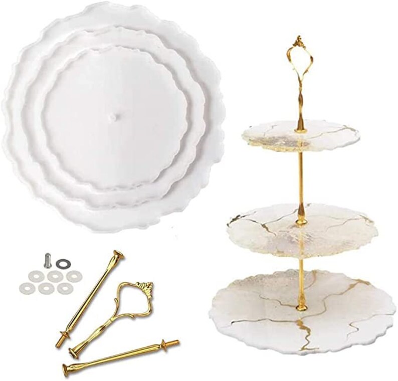 May include: A white, three-tiered serving tray with gold-coloured hardware. The tray has a wavy edge design. The hardware includes a handle and connecting rods. Also included are the components to assemble the tray.