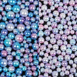 Puede incluir: Un surtido de perlas iridiscentes en varios tama&ntilde;os y colores, incluyendo azul, morado y rosa. Las perlas tienen un acabado brillante y est&aacute;n dispersas sobre una superficie oscura, creando un efecto brillante. Ideal para la creaci&oacute;n de joyas o proyectos de artesan&iacute;a.