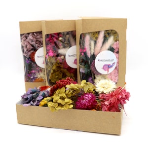 Peut inclure: Trois bo&icirc;tes en papier kraft avec des fen&ecirc;tres transparentes remplies de fleurs s&eacute;ch&eacute;es et une bo&icirc;te rectangulaire de fleurs s&eacute;ch&eacute;es de diff&eacute;rentes couleurs. Les bo&icirc;tes ont un autocollant avec l'inscription "KUNSTHARZ.ART". Les fleurs sont roses, violettes, jaunes et rouges.