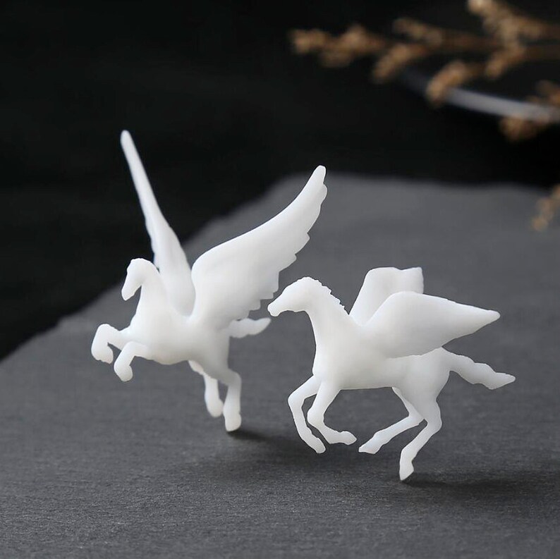 May include: Two white Pegasus figurines, one with wings spread and the other in a running pose. The mythical creatures are set against a dark background, highlighting their detailed form and elegant design. These figurines are ideal for home decor.