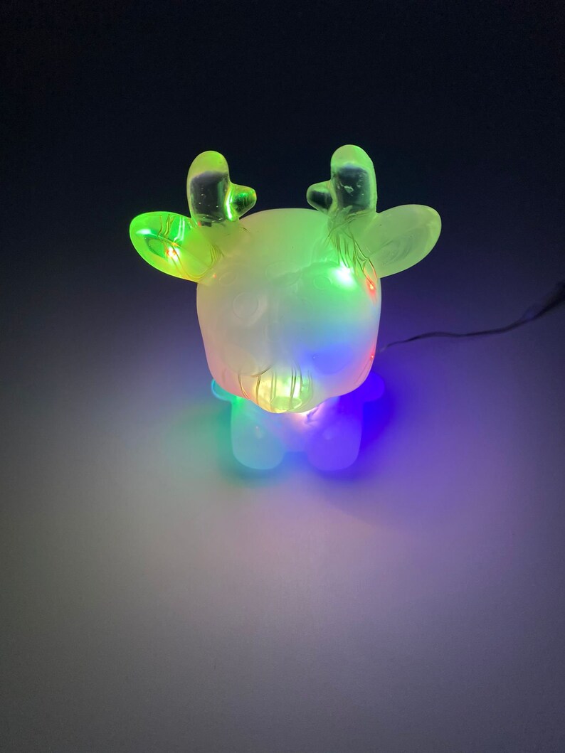 May include: A glowing reindeer figurine with a frosted body and clear antlers. The reindeer is illuminated by colorful LED lights, creating a festive and whimsical display. The lights cycle through green, blue, and other colors.