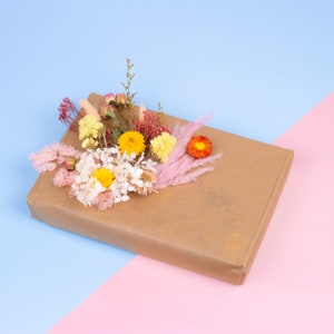 Peut inclure: Un colis rectangulaire envelopp&eacute; dans du papier brun, orn&eacute; d'une composition florale. Les fleurs comprennent des fleurs jaunes, oranges, roses et blanches, cr&eacute;ant un accent color&eacute;. Le fond est divis&eacute; en diagonale, avec des sections bleues et roses.