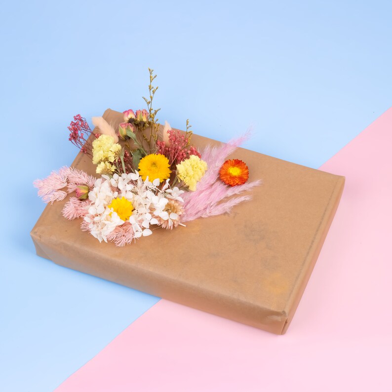 Peut inclure: Un colis rectangulaire envelopp&eacute; dans du papier brun, orn&eacute; d'une composition florale. Les fleurs comprennent des fleurs jaunes, oranges, roses et blanches, cr&eacute;ant un accent color&eacute;. Le fond est divis&eacute; en diagonale, avec des sections bleues et roses.