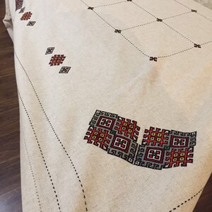 May include: A white linen tablecloth with black and red embroidered geometric patterns. The tablecloth has a black stitched border.