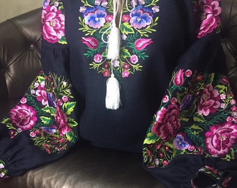 May include: A black embroidered blouse with a floral design. The embroidery features pink, blue, and green flowers. The blouse has a white tassel tie at the neckline.