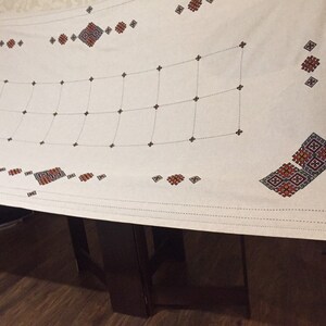 May include: White tablecloth with a grid pattern and red and black embroidered designs.