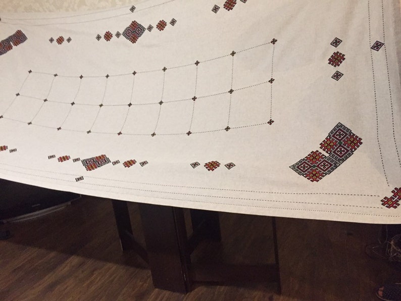 May include: White tablecloth with a grid pattern and red and black embroidered designs.