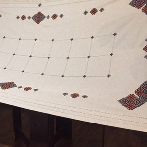 May include: White tablecloth with a grid pattern and embroidered red, black, and white geometric designs.