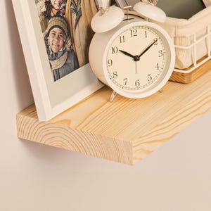 May include: A light-colored wooden shelf with a white framed photo and a white alarm clock. The clock shows the time as 9:50. A small white basket sits on a wooden tray.