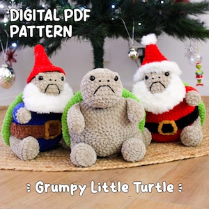 Op de afbeelding: Drie gehaakte schildpadknuffels met chagrijnige gezichten. Twee zijn verkleed als kerstman, een in een rode hoed en jas, de andere in een blauwe outfit. De derde schildpad is effen grijs. Tekst luidt "DIGITAL PDF PATTERN" en ": Grumpy Little Turtle :".
