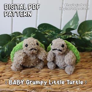 May include: Two handmade crochet turtles with grumpy expressions. The turtles are light brown with green shells. The image includes the text "DIGITAL PDF PATTERN" and "BABY Grumpy Little Turtle". The background features green leaves.