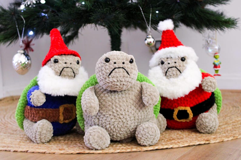 May include: Three crocheted turtle plushies, each with a sad expression. One is dressed as a gnome in a red hat and blue outfit, another is plain gray, and the third is in a Santa Claus outfit with a red hat and white beard.