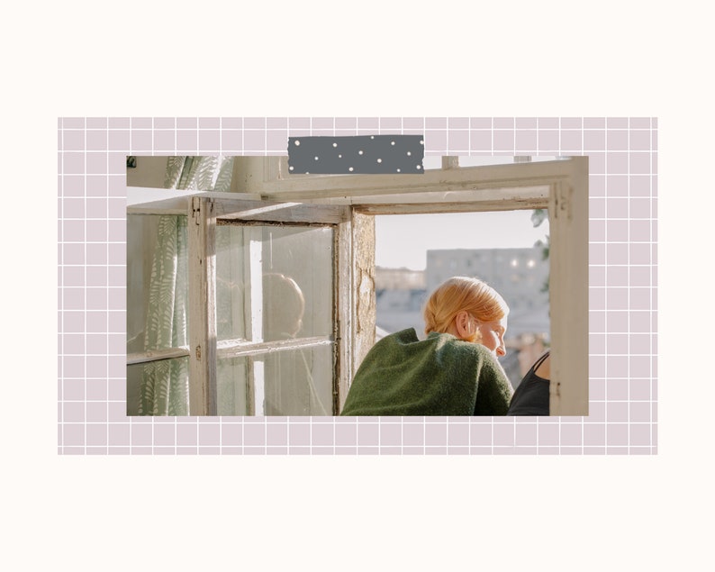 May include: A person with red hair sits by a window looking out at a cityscape. The window is old and has multiple panes. The person is wearing a green sweater.