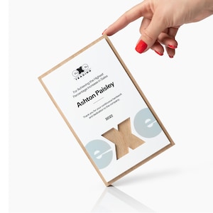 May include: A wooden plaque with a white face and a light brown border. The plaque has the text "For Achieving the Highest Percentage Increase in Sales" and "Ashton Paisley". The year "2022" is also visible.