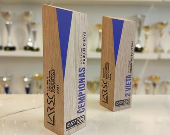 May include: Two wooden trophies with a blue and white accent. The trophies have text that reads "ČEMPIONAS" and "2 VIETA". The trophies are for the "LIETUVOS AUTOMOBILIŲ RALIO SPRINTO ČEMPIONATAS 2021".