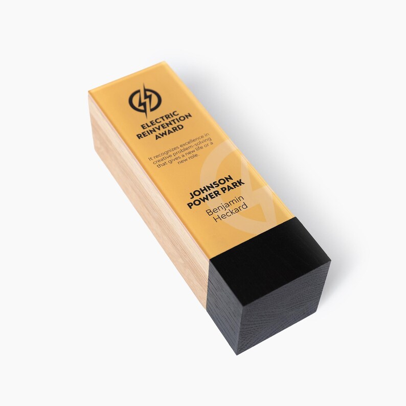 May include: A rectangular award with a wooden base and a yellow top. The top features the text "ELECTRIC REINVENTION AWARD" and "JOHNSON POWER PARK, Benjamin Heckard". The award has a black bottom section and a lightning bolt logo.