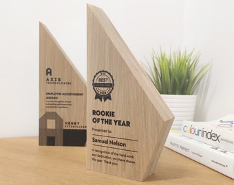 May include: Two wooden awards with geometric designs. One reads "AXIS TECHNOLOGIES EMPLOYEE ACHIEVEMENT AWARD" and the other says "ROOKIE OF THE YEAR" with the recipient's name. The awards are light brown with black text.