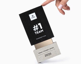 May include: A black box with the Ferro logo and the words "#1 TEAM MARKETING" in white. The box is partially open, revealing a concrete-like block with the text "PROUD I FOCUSED I UNITED" and the year "2025".