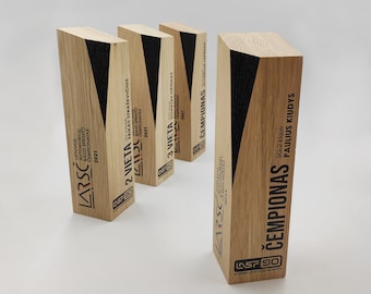 May include: Four wooden awards with black accents and text in Lithuanian. The awards are for first, second, and third place in a rally sprint championship, and the champion. The text on the awards reads "LARSC", "LIETUVOS AUTOMOBILIŲ RALIO SPRINTO ČEMPIONATAS 2021", "2 VIETA", "3 VIETA", and "ČEMPIONAS".
