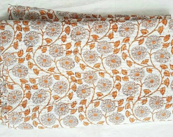 Puede incluir: Edredón plegado con un diseño floral blanco y naranja. El patrón presenta grandes flores y hojas estilizadas en tonos naranja y marrón. El edredón está doblado, mostrando el patrón y los detalles de las costuras. El fondo es blanco.