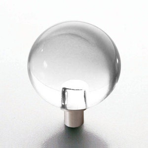 May include: A clear, spherical cabinet knob with a silver-colored stem. The knob is transparent, allowing light to pass through. The design is simple and modern, suitable for various furniture styles.