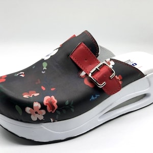 May include: Black clog-style shoe with a floral pattern in red, pink, and white. The shoe features a red strap with a silver buckle and a white sole. Designed for comfort and support.