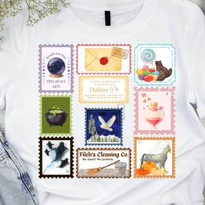 May include: White t-shirt featuring a collection of colorful postage stamp designs. The stamps depict various whimsical illustrations, including a crystal ball, a cauldron, and a potion bottle. The shirt is paired with denim jeans and white sneakers.