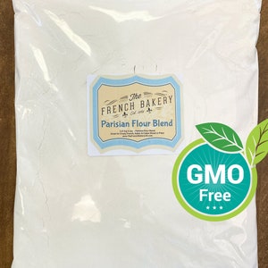 May include: A clear plastic bag filled with white Parisian Flour Blend. The label reads "The French Bakery" and "GMO Free". The bag contains 2.27 kg of flour, perfect for crusty French, Italian, and Cuban bread or pizza.