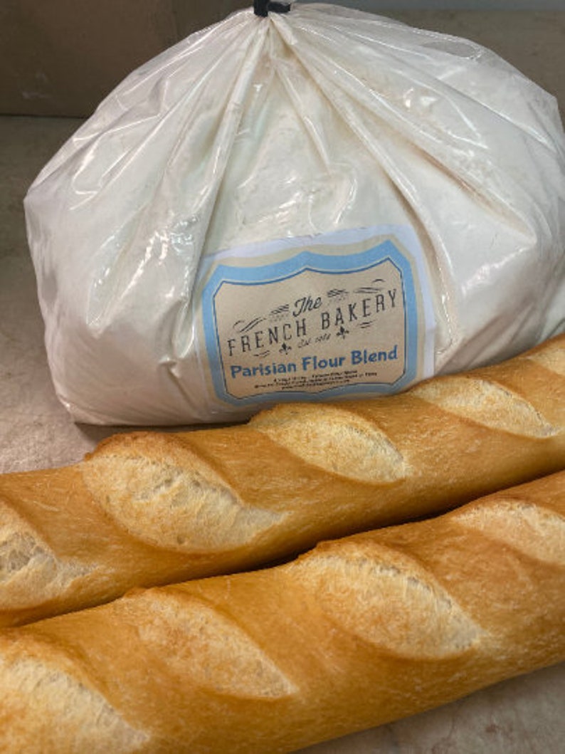 May include: A large white bag of The French Bakery Parisian Flour Blend, next to two long, golden brown baguettes.