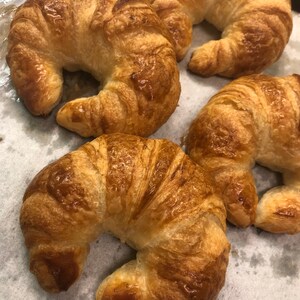 May include: Four golden brown croissants on a white parchment paper surface. The croissants are arranged in a semi-circle.