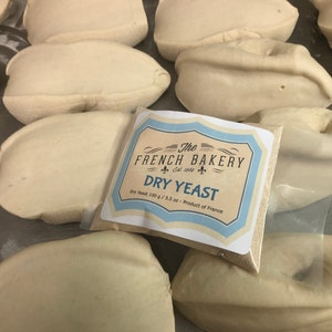 May include: A white bag of dry yeast with a blue and white label that reads "The French Bakery Est. 1964 Dry Yeast Dry Yeast 100 g / 3.5 oz - Product of France".