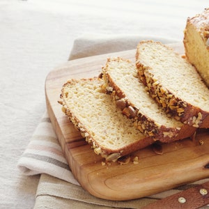May include: A loaf of sliced bread with nuts and seeds on a wooden cutting board. The bread is light brown and the nuts and seeds are a variety of colors.