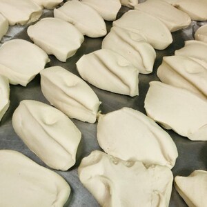 May include: A close-up of a metal surface with multiple white dough balls arranged in rows. The dough balls are smooth and slightly rounded.