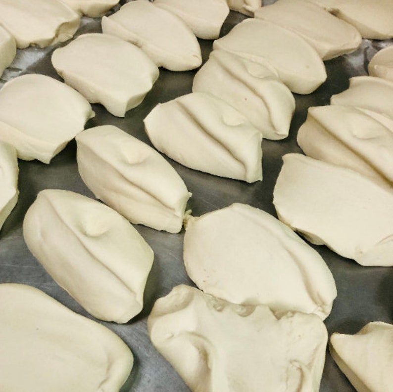 May include: A close-up of a metal surface with multiple white dough balls arranged in rows. The dough balls are smooth and slightly rounded.