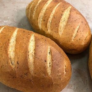 May include: Three loaves of freshly baked bread with a golden brown crust and a slightly cracked surface. The bread has a rustic appearance and is likely made with whole wheat flour.