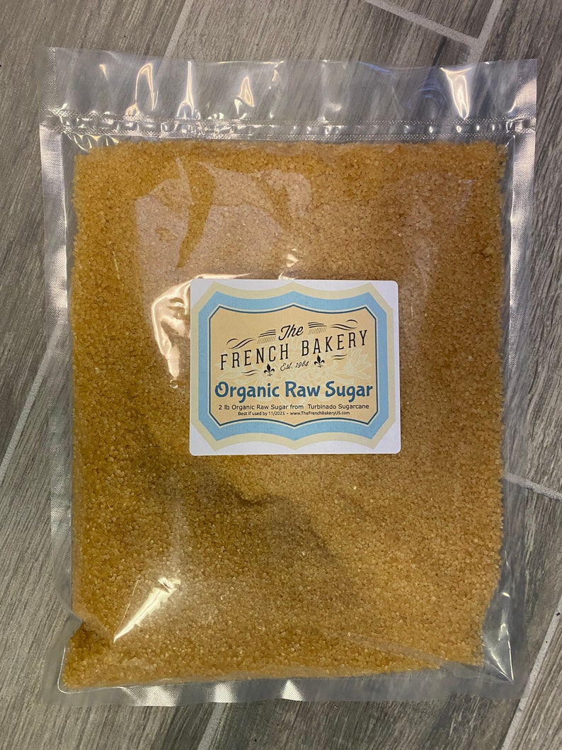 May include: A clear plastic bag filled with 2 pounds of organic raw sugar from The French Bakery. The bag has a label with the company's logo and the text "Organic Raw Sugar".