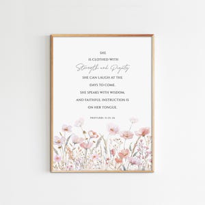 May include: Framed print featuring the text "She is clothed with Strength and Dignity" with a floral border. The artwork includes a watercolor design of pink and peach flowers and greenery. The text is from Proverbs 31:25-26.