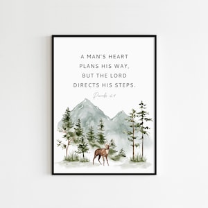 May include: A watercolor print with a mountain landscape, a deer, and the quote "A man's heart plans his way, but the Lord directs his steps." with the scripture reference "Proverbs 16:9".