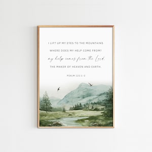 May include: Framed art print featuring a watercolor landscape with mountains, trees, and a river. The artwork includes the text "I lift up my eyes to the mountains..." and Psalm 121:1-2. The frame is a light brown color.