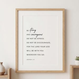 Puede incluir: Una impresión de arte mural enmarcada que presenta el versículo bíblico Josué 1:9 en texto negro sobre un fondo blanco. El texto dice: Be strong and courageous. Do not be afraid; do not be discouraged, for the Lord your God will be with you.