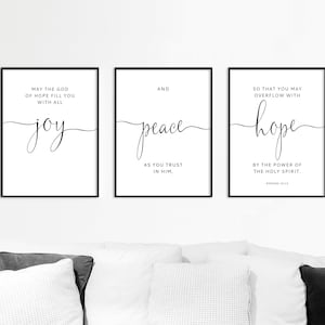 Może przedstawiać: Trzy oprawione wydruki artystyczne z czarnymi ramkami i białym tłem. Każdy wydruk zawiera elegancki tekst kursywą: "joy", "peace" i "hope". Wydruki zawierają również dodatkowy tekst z Rzymian 15:13.