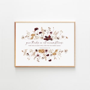 May include: A framed print with a floral design in shades of burgundy, cream, and gold. The print features the text "give thanks in all circumstances: FOR THIS IS GOD'S WILL FOR YOU IN CHRIST JESUS. 1 THESSALONIANS 5:18"
