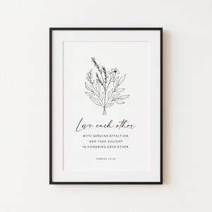 May include: A framed wall art print featuring a black line drawing of a floral bouquet centered above the text: Love each other WITH GENUINE AFFECTION, AND TAKE DELIGHT IN HONORING EACH OTHER. ROMANS 12:10. The design is black on a white background.