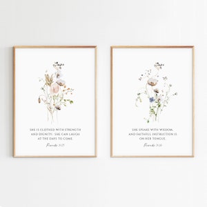 Könnte beinhalten: Zwei gerahmte Drucke mit Aquarell-Blumenillustrationen und Bibelversen. Der linke Druck zeigt einen Blumenstrauß in Braun-, Rosa- und Weißtönen mit dem Text "Sie ist mit Stärke und Würde bekleidet: Sie kann über die kommenden Tage lachen. Sprichwörter 31:25". Der rechte Druck zeigt einen Blumenstrauß in Blau-, Weiß- und Grüntönen mit dem Text "Sie spricht mit Weisheit. Und treue Unterweisung ist auf ihrer Zunge. Sprichwörter 31:26".