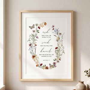 Puede incluir: Una lámina de arte enmarcada con una corona floral que rodea el texto: ask AND IT WILL BE GIVEN TO YOU seek AND YOU WILL FIND knock AND THE DOOR WILL BE OPENED TO YOU MATTHEW 7:7. La corona incluye flores silvestres coloridas y dos mariposas.