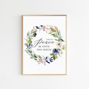 Op de afbeelding: Een aquarelprint met een bloemenkrans in tinten blauw, groen en roze. De krans omringt de tekst "Vrede zij dit huis" met de bijbelverwijzing "Lukas 10:5" boven de tekst.